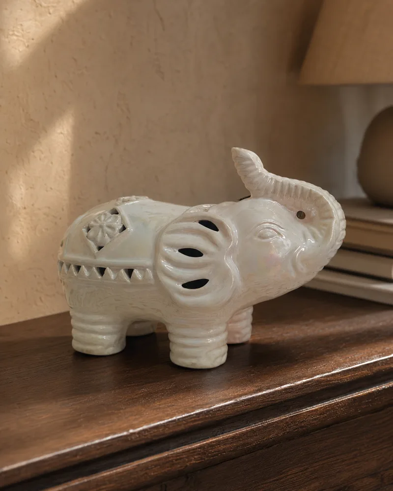 Pearlescent ivory ceramic elephant with pierced lattice details on a walnut console