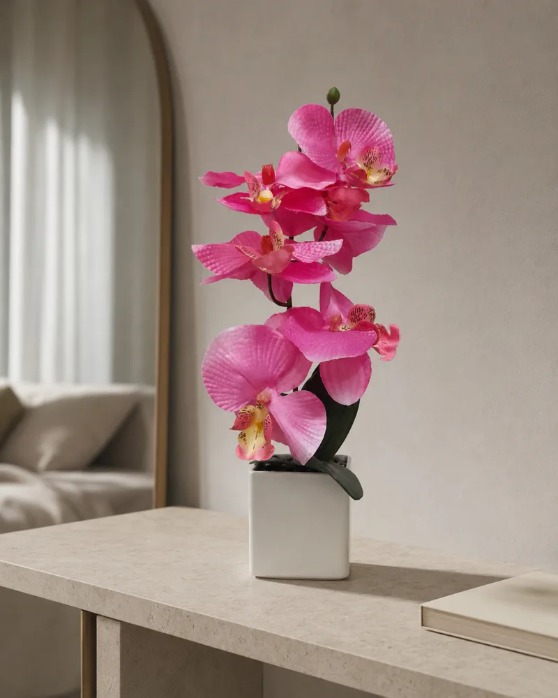 Faux pink orchid arrangement in a white ceramic pot on a stone console